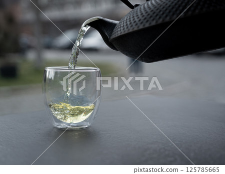 Pouring green tea into a glass from a metal kettle on blurred background, hot drink in teapot 125785665