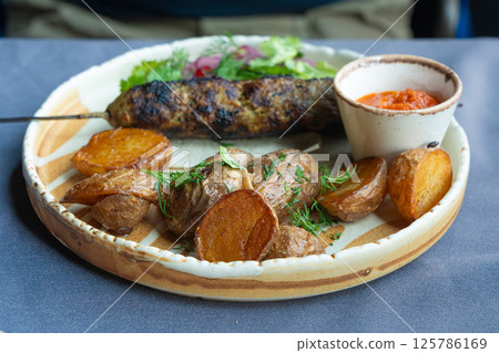 Georgian lula kebab plate. Bbq skewer, traditional barbecue dish with baked potatoes, sauce 125786169