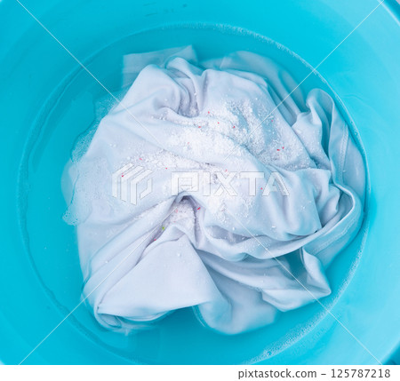 Hand laundry washing clothes in blue plastic basin with detergent powder and oxygen bleach 125787218