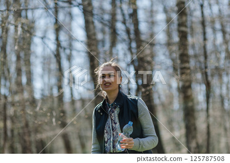 A young woman drinking water in the forest. A woman resting in a park and drinking mineral water from a plastic bottle 125787508