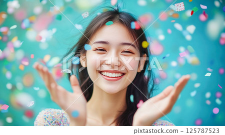 Happy young Asian woman having fun surrounded by colorful confetti 125787523