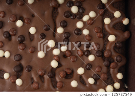 Chocolate brownie cake texture background sprinkled with white and dark balls, brounie banner 125787549