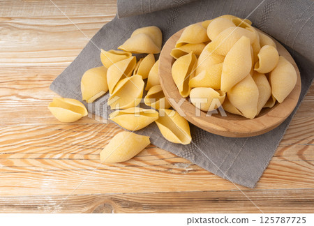 Raw conchiglioni pasta in wood bowl. Dry conchiglie noodle in shell shape Raw conchiglioni pasta in wood bowl. Dry conchiglie noodle in shell shape 125787725
