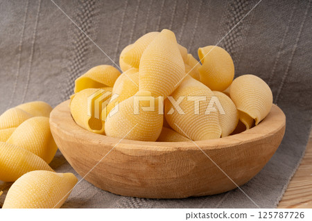 Raw conchiglioni pasta in wood bowl. Dry conchiglie noodle in shell shape Raw conchiglioni pasta in wood bowl. Dry conchiglie noodle in shell shape 125787726