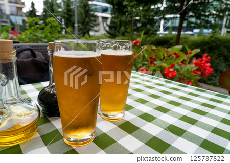 Two beer glasses at outdoor cafe, cold pint glass on checkered tablecloth table, cool condensation Two beer glasses at outdoor cafe, cold pint glass on checkered tablecloth table, cool condensation 125787822