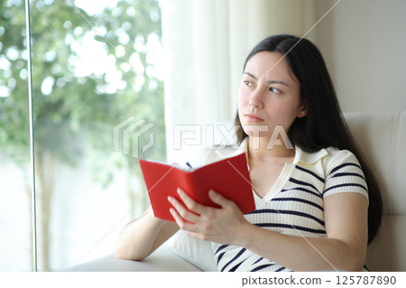 Serious asien woman holding agenda and thinking Serious asien woman holding agenda and thinking 125787890