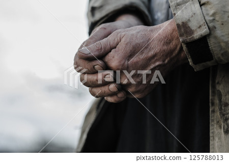 The worker's hands are rough and covered in dirt, showing years of hard labor. His hands bear deep wrinkles and calluses. 125788013