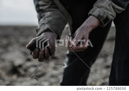 The hands of a weary farmer cradle the soil with care. The hands are rough and cracked from years of labor.  125788030