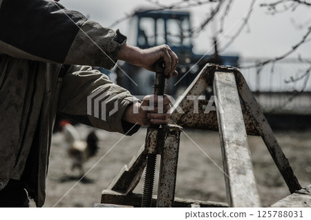 A pensioner repairs a trailer for a tractor. His hands shake from exhaustion.  125788031