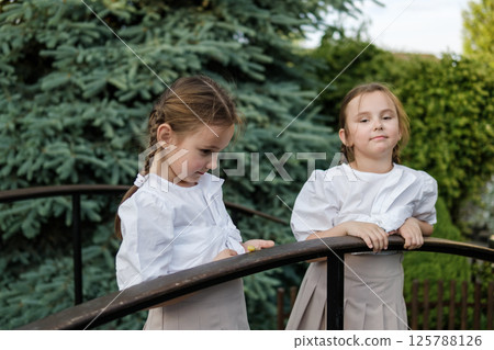A pair of girls carefully follow every movement of the snail. Both have neatly braided hair, and their outfits look festive 125788126