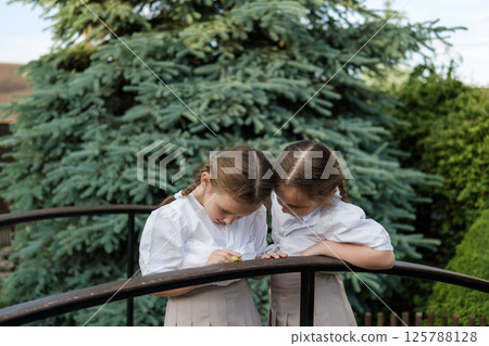 Little girls carefully examine a snail on the wooden railing. Light blouses and matching skirts create a sense of gentle symmetry.  125788128