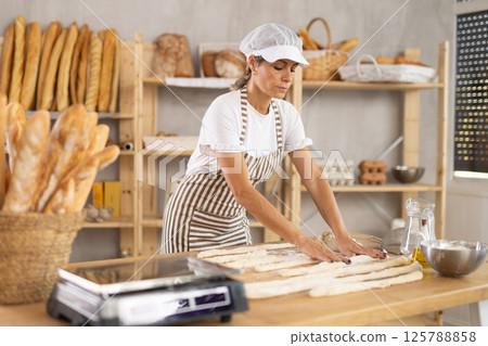 Elderly woman baker rolls out dough Elderly woman baker rolls out dough 125788858