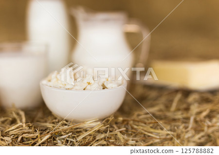 Milk, cottage cheese, cream, cheese on table against the background of hay Milk, cottage cheese, cream, cheese on table against the background of hay 125788882