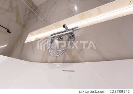 A modern chrome shower faucet on marble wall in a clean minimalist bathroom A modern chrome shower faucet on marble wall in a clean minimalist bathroom 125789142