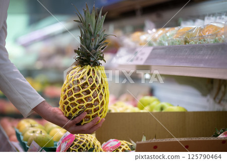 Shopper's hands choosing a pineapple Shopper's hands choosing a pineapple 125790464