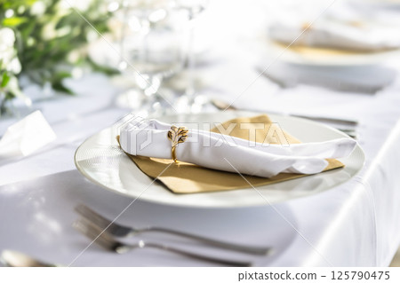 A wedding table covered with a white tablecloth, decorated with flowers, candles, glasses and cutlery A wedding table covered with a white tablecloth, decorated with flowers, candles, glasses and cutlery 125790475
