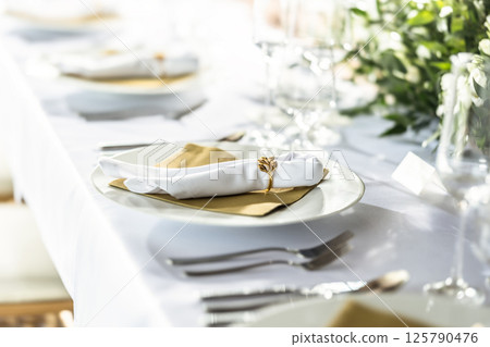 A wedding table covered with a white tablecloth, decorated with flowers, candles, glasses and cutlery 125790476