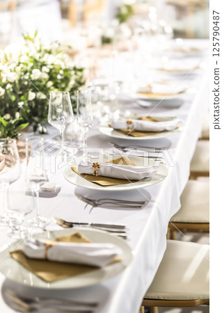 A wedding table covered with a white tablecloth, decorated with flowers, candles, glasses and cutlery A wedding table covered with a white tablecloth, decorated with flowers, candles, glasses and cutlery 125790487