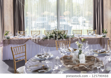 A wedding table covered with a white tablecloth, decorated with flowers, candles, glasses and cutlery A wedding table covered with a white tablecloth, decorated with flowers, candles, glasses and cutlery 125790488