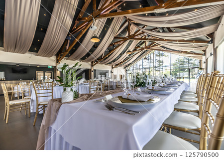 Wedding setting and decorated tables in a beautiful modern interior of a performance hall with a modern light ceiling of wooden construction 125790500