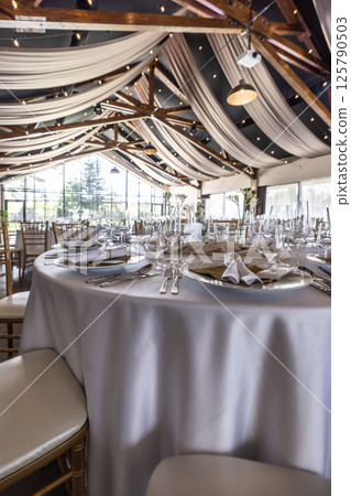 Wedding setting and decorated tables in a beautiful modern interior of a performance hall with a modern light ceiling of wooden construction 125790503