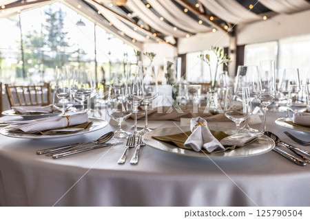 Wedding setting and decorated tables in a beautiful modern interior of a performance hall with a modern light ceiling of wooden construction Wedding setting and decorated tables in a beautiful modern interior of a performance hall with a modern light ceiling of wooden construction 125790504