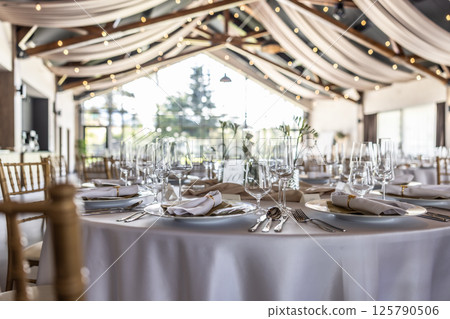 Wedding setting and decorated tables in a beautiful modern interior of a performance hall with a modern light ceiling of wooden construction Wedding setting and decorated tables in a beautiful modern interior of a performance hall with a modern light ceiling of wooden construction 125790506