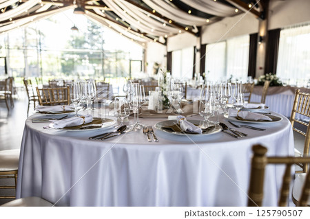 Wedding setting and decorated tables in a beautiful modern interior of a performance hall with a modern light ceiling of wooden construction Wedding setting and decorated tables in a beautiful modern interior of a performance hall with a modern light ceiling of wooden construction 125790507