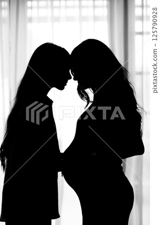 Silhouette of daughter and pregnant mother hugging each other against window background 125790928