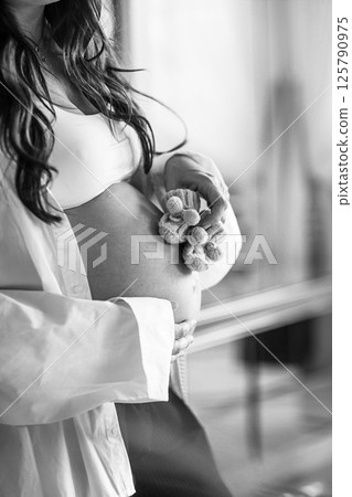 Beautiful pregnant woman at home. Closeup little shoes for baby in hands Beautiful pregnant woman at home. Closeup little shoes for baby in hands 125790975