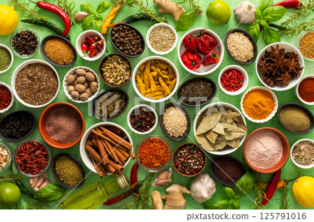 A colorful assortment of fresh, fragrant spices and herbs displayed on a soft green background, capturing a vibrant culinary essence 125791016