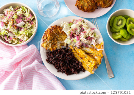 A healthy breakfast featuring brown rice with baked white fish, zucchini-carrot pancakes, Chinese cabbage salad with radish, and a refreshing kiwi dessert for a balanced, nutritious start to the day 125791021