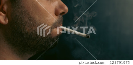 Close up of bearded man smoking a cigarette on black background. 125791975