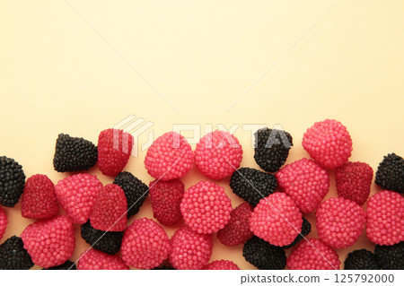 Red chewing sweets in the form of berries. Sweets in the form of raspberries on beige background. Space for text 125792000