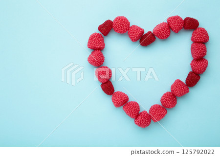 Red chewing sweets in the form of heart. Sweets in the form of raspberries on blue background. Space for text 125792022