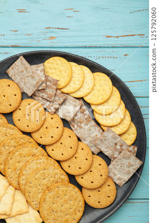 Different crackers on plate on blue wooden background. Vertical photo 125792060