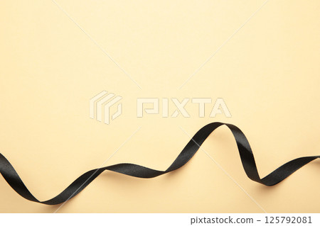 Black satin ribbon on beige background, top view 125792081