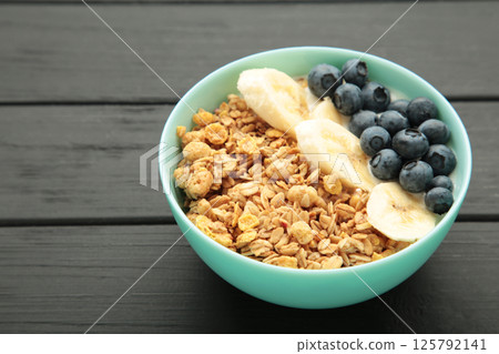 Oat raisin granola with fresh summer berries in a bowl on black wooden background. Concept of healthy breakfast food, clean eating, dieting 125792141