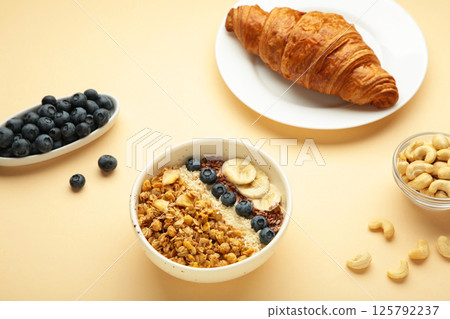 Beautiful morning breakfast with fresh croissants and granola with yoghurt on beige background. Tasty and healthy breakfast 125792237