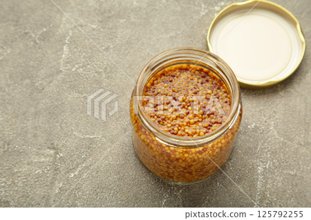 Glass jar of wholegrain mustard on grey concrete background 125792255