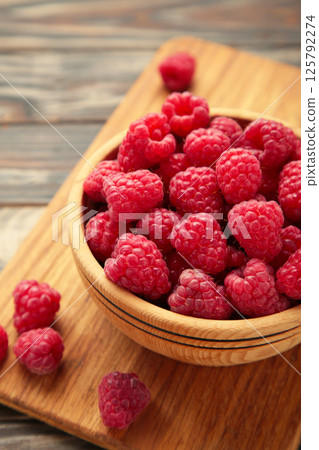 Raspberries in wooden bowl on brown background. Vertical photo 125792274