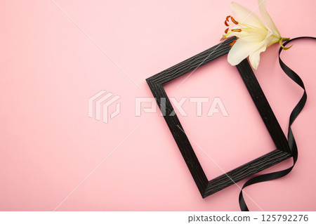 Beautiful lily flower with blank frame and black funeral ribbon on pink background Beautiful lily flower with blank frame and black funeral ribbon on pink background 125792276