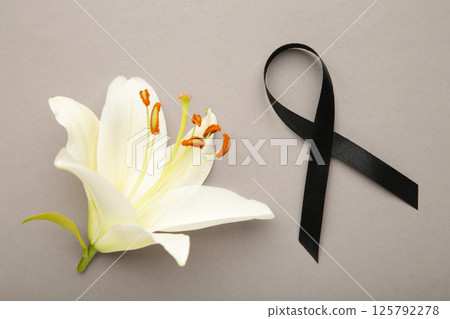 White liles flowers with black ribbon on grey. Mourning or funeral background White liles flowers with black ribbon on grey. Mourning or funeral background 125792278
