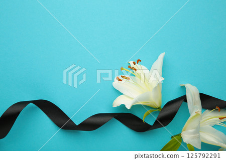 White liles flowers with black ribbon on blue. Mourning or funeral background 125792291