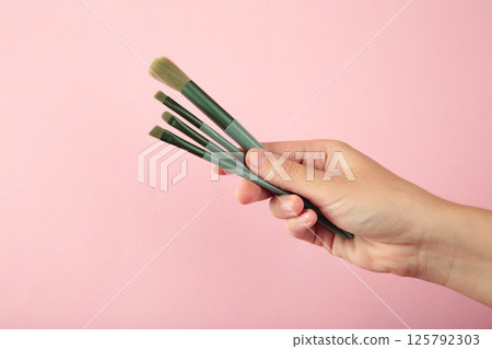 Female hand with make-up artist brush on pink background 125792303