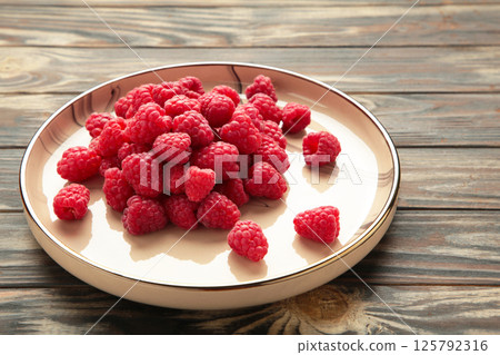 Raspberries on beige plate on brown wooden background Raspberries on beige plate on brown wooden background 125792316