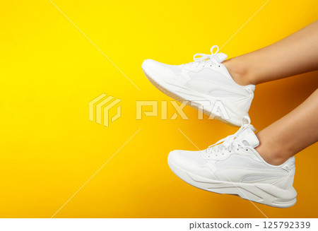 Female legs in stylish white sneakers on yellow background. Space for text 125792339