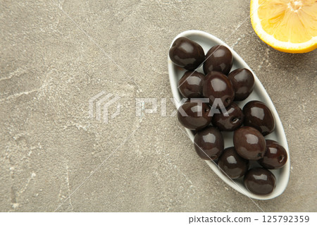 Fresh olives in white plate with lemon on grey concrete background. 125792359