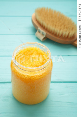 Handmade Sugar Peach Scrub With Argan Oil. Scrub with massage brush on blue background Handmade Sugar Peach Scrub With Argan Oil. Scrub with massage brush on blue background 125792373