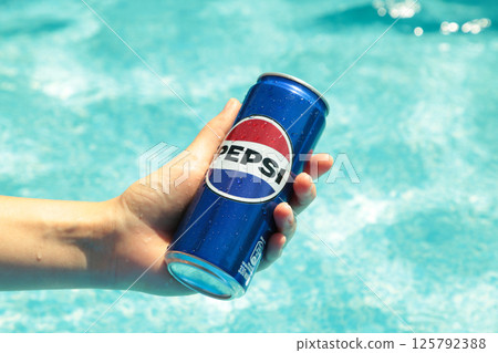 Mykolaiv, Ukraine - June 2024: Can with cold drink Pepsi in the hand against the backdrop of the pool on a hot day. Summer vacation concept 125792388
